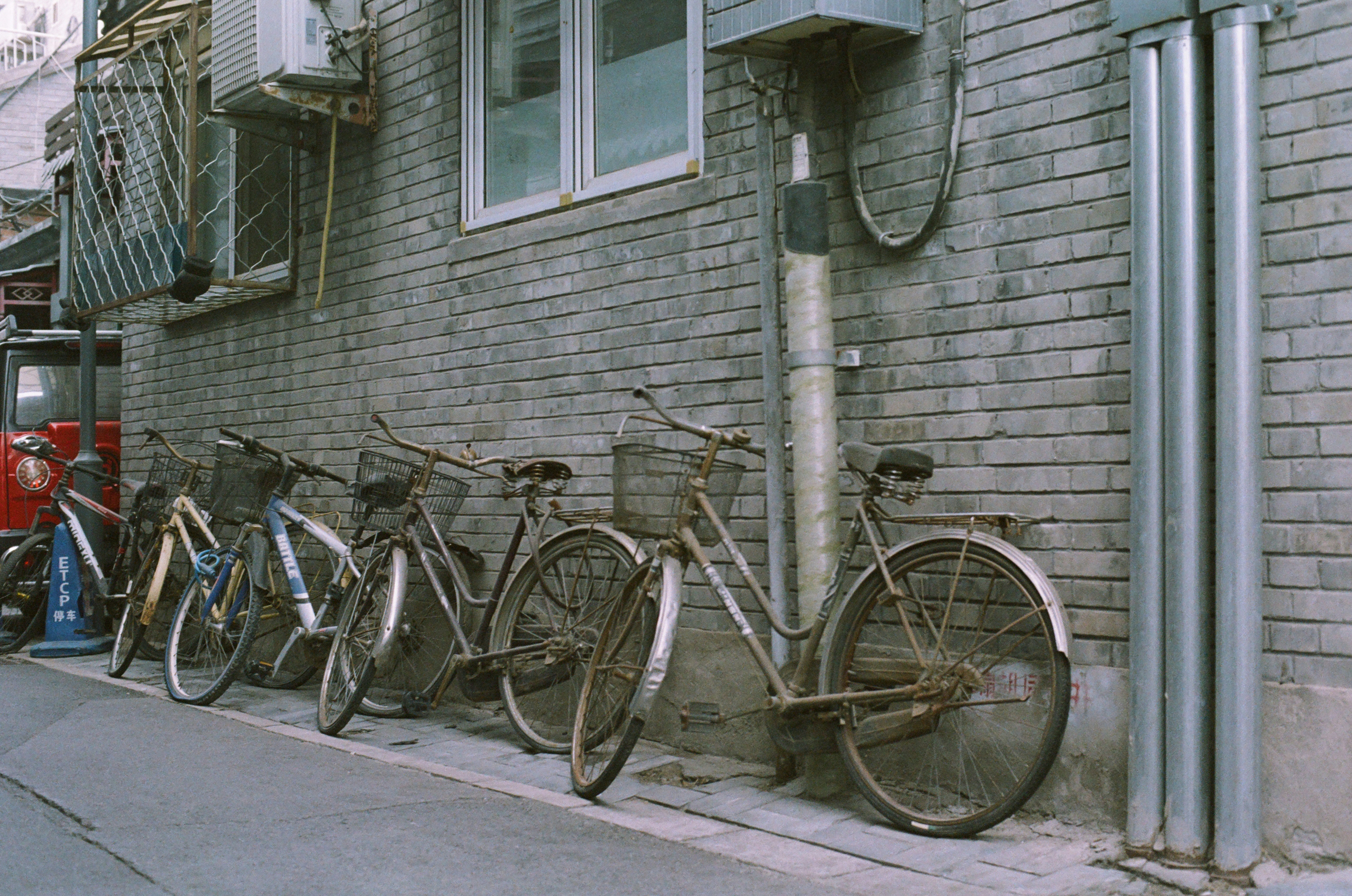 There are a lot of abandoned bikes in the alley, and depending on the extent of the damage, it's hard to guess if their owners are still alive. (Film: Kodak Gold 200 that has expired for 16 years) by Bike Brands a row of bikes parked next to a brick building